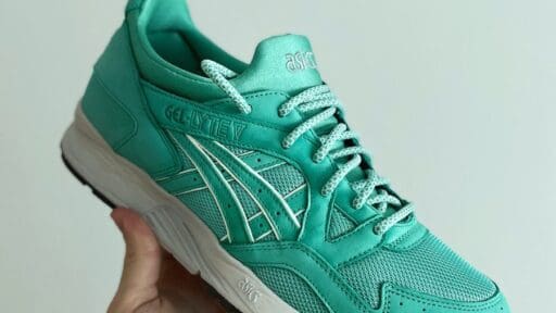 person holding green asics athletic shoe