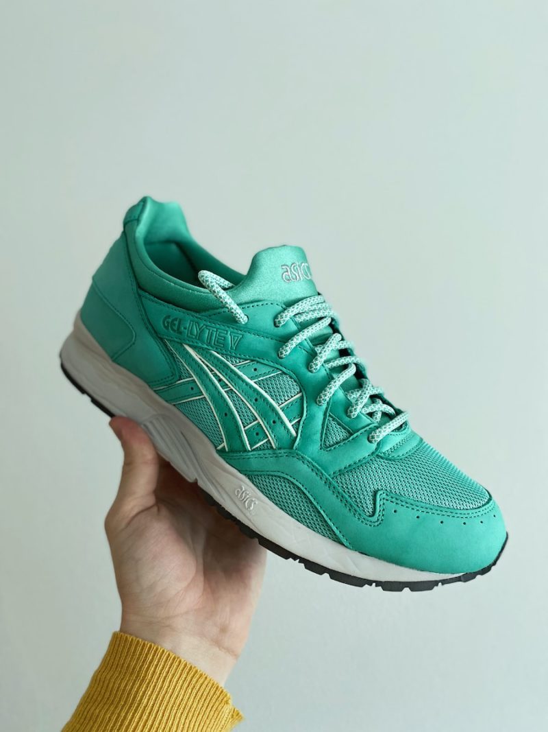 person holding green asics athletic shoe