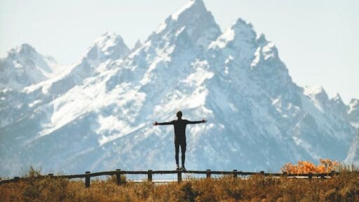 man standing on fence overlooking mountain in backcountry