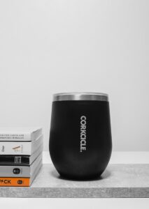 A black corkcicle cup sitting on top of a table next to a stack of books