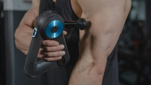Close-up of a man using a massage gun for muscle relaxation on his arm.