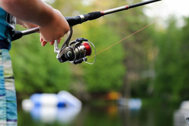 person holding fishing reel next to tackle box