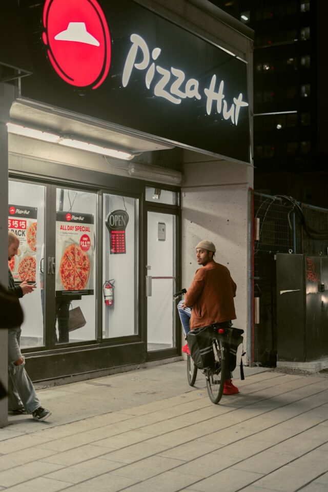 a man riding a bike past a pizza hut